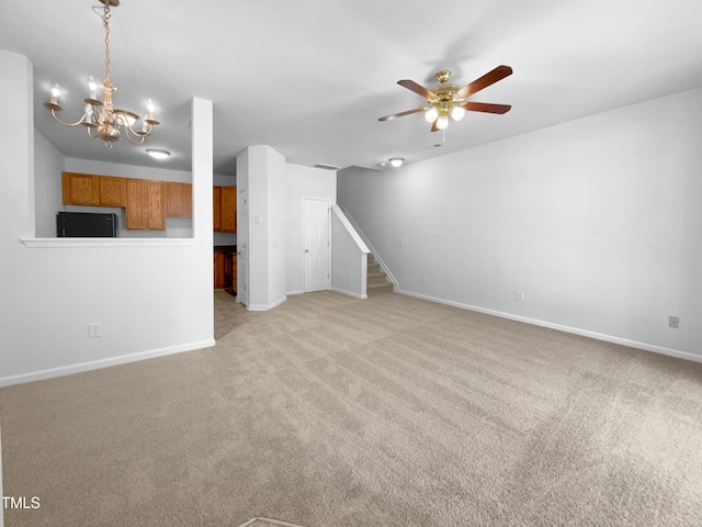 unfurnished living room featuring light colored carpet, stairs, ceiling fan with notable chandelier, and baseboards