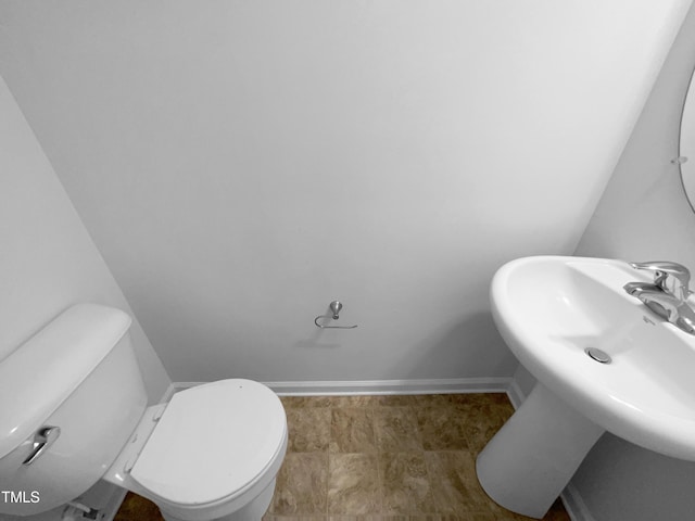half bathroom featuring baseboards, a sink, and toilet