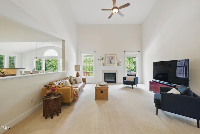 carpeted living room with a fireplace with flush hearth, high vaulted ceiling, ceiling fan, and baseboards