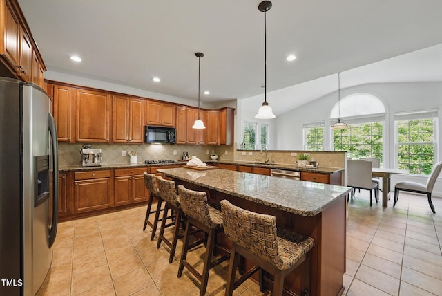 kitchen with brown cabinets, light tile patterned flooring, appliances with stainless steel finishes, a sink, and vaulted ceiling