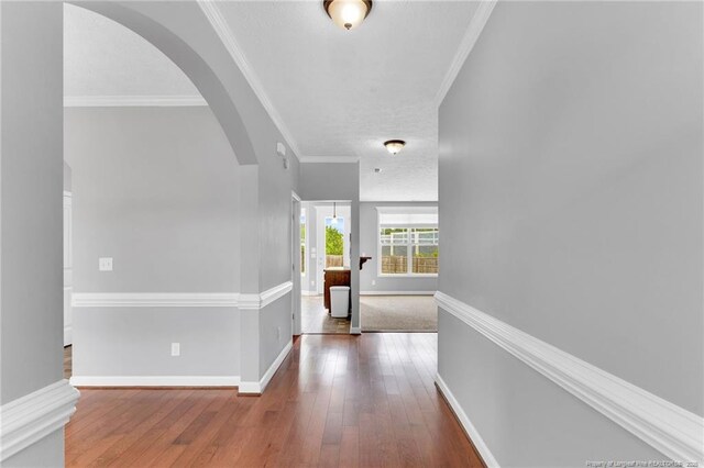 corridor featuring ornamental molding, hardwood / wood-style floors, baseboards, a textured ceiling, and arched walkways