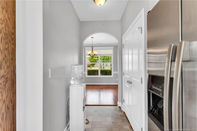 hall featuring baseboards, stone finish floor, arched walkways, and a chandelier