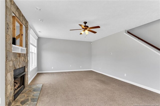 unfurnished living room featuring baseboards, ceiling fan, a fireplace, and carpet flooring