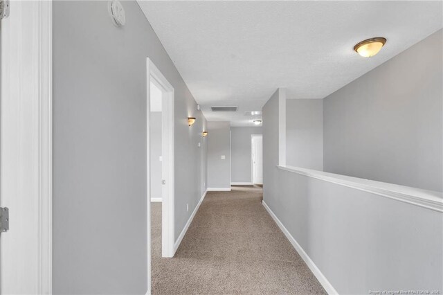 hall with carpet floors, a textured ceiling, and baseboards