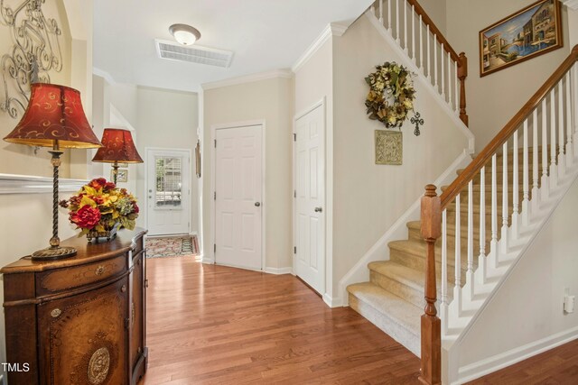 entrance foyer with crown molding, light wood-style floors, stairs, baseboards, and visible vents