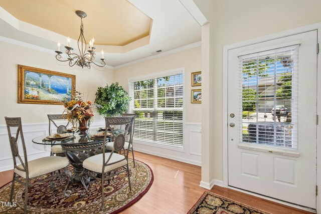 dining room featuring crown molding, a wainscoted wall, a chandelier, light wood-style floors, and a tray ceiling