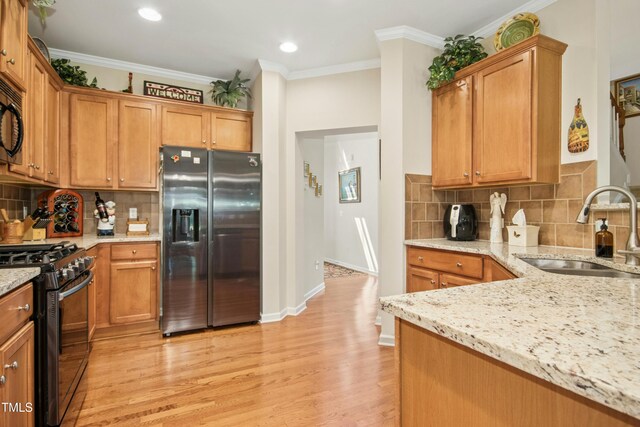 kitchen featuring light stone countertops, tasteful backsplash, a sink, light wood finished floors, and black appliances