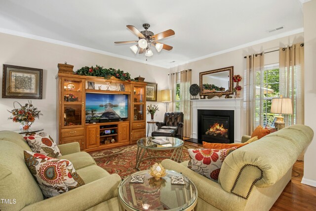 living area with visible vents, ornamental molding, wood finished floors, ceiling fan, and a fireplace with flush hearth
