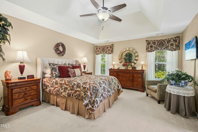 bedroom with a raised ceiling, ceiling fan, and light carpet