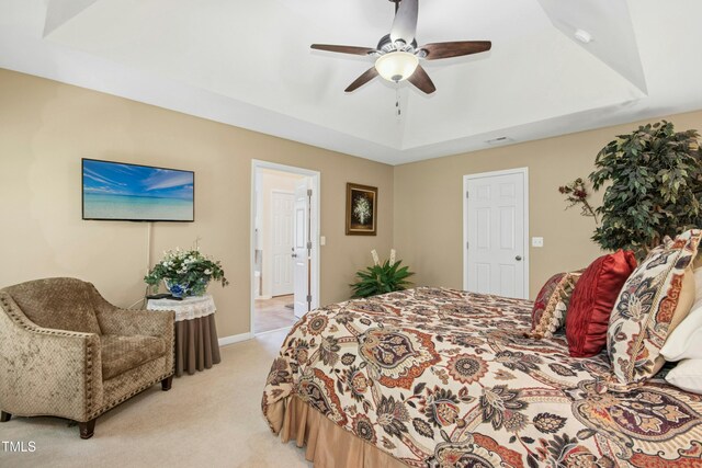 bedroom with a ceiling fan, a tray ceiling, light carpet, and baseboards