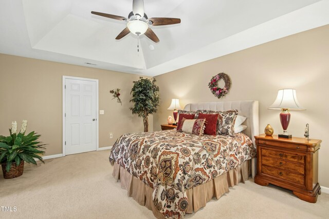bedroom featuring ceiling fan, light colored carpet, baseboards, a tray ceiling, and visible vents