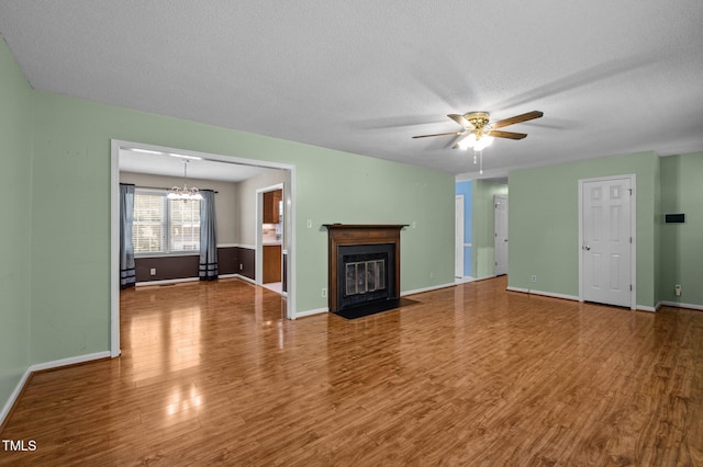 unfurnished living room featuring baseboards, a textured ceiling, wood finished floors, and ceiling fan with notable chandelier