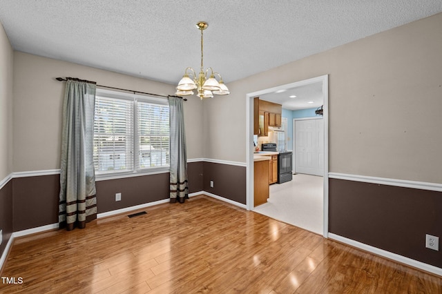 unfurnished dining area featuring an inviting chandelier, light wood finished floors, a textured ceiling, and visible vents
