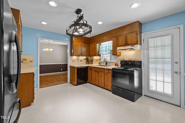 kitchen featuring light countertops, under cabinet range hood, brown cabinets, a sink, and black appliances