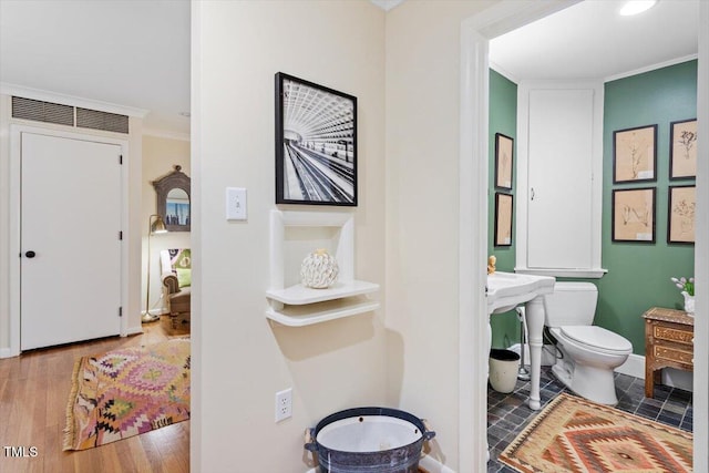 bathroom featuring crown molding, toilet, baseboards, and wood finished floors