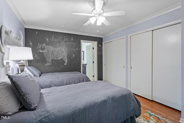 bedroom featuring ornamental molding, a ceiling fan, two closets, and wood finished floors