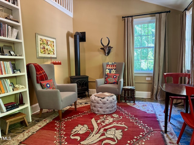 sitting room featuring baseboards, a wood stove, and vaulted ceiling