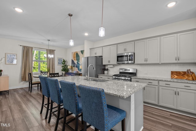 kitchen featuring a kitchen island with sink, backsplash, appliances with stainless steel finishes, a sink, and a breakfast bar