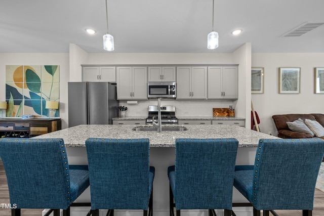 kitchen featuring a sink, an island with sink, stainless steel appliances, tasteful backsplash, and visible vents