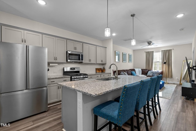 kitchen featuring appliances with stainless steel finishes, a breakfast bar, a sink, gray cabinets, and visible vents