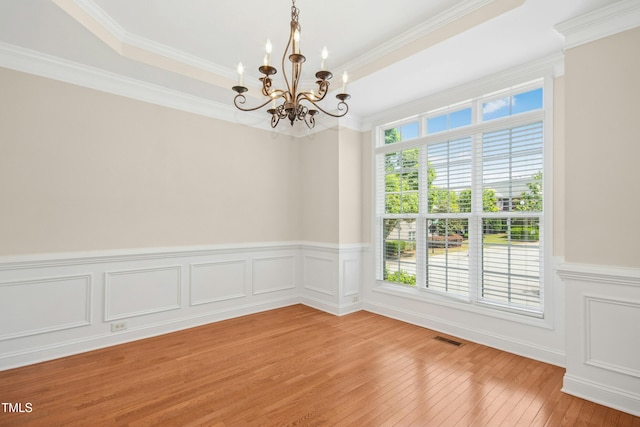 spare room featuring visible vents, light wood-type flooring, a wainscoted wall, a notable chandelier, and ornamental molding