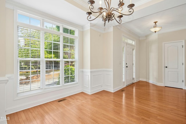 interior space with crown molding, light wood finished floors, a chandelier, a wainscoted wall, and visible vents