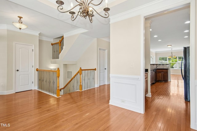interior space featuring visible vents, crown molding, a notable chandelier, light wood finished floors, and an upstairs landing