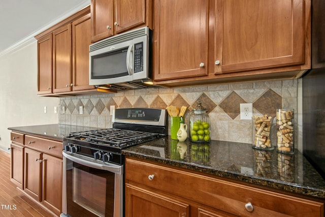 kitchen featuring brown cabinetry, dark stone countertops, tasteful backsplash, and stainless steel appliances