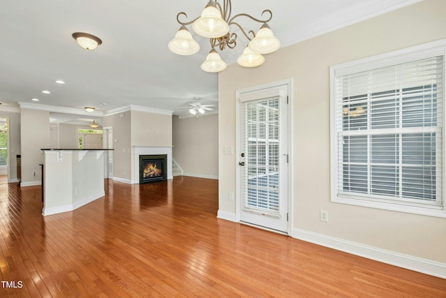 unfurnished living room featuring hardwood / wood-style flooring, baseboards, ceiling fan with notable chandelier, a glass covered fireplace, and ornamental molding