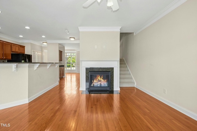 unfurnished living room with baseboards, ornamental molding, ceiling fan, and light wood finished floors