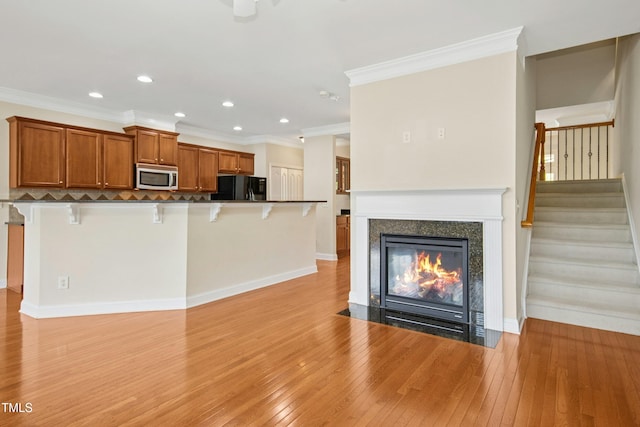 unfurnished living room featuring crown molding, a fireplace with flush hearth, stairway, light wood finished floors, and recessed lighting