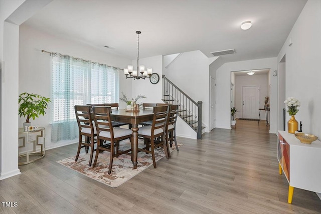 dining space featuring light wood finished floors, a chandelier, stairway, and baseboards
