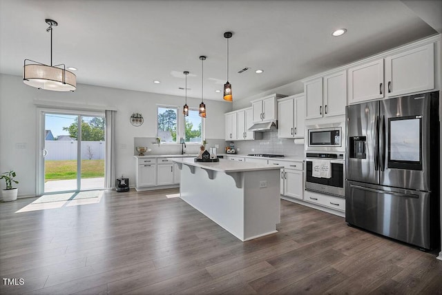 kitchen with appliances with stainless steel finishes, under cabinet range hood, light countertops, white cabinetry, and a center island