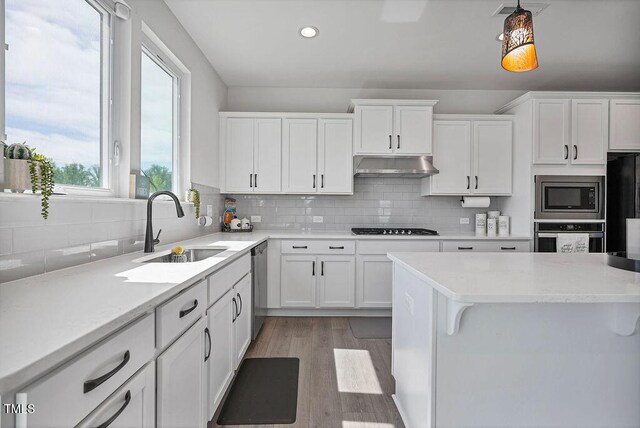 kitchen featuring black appliances, a sink, under cabinet range hood, white cabinets, and light wood-type flooring