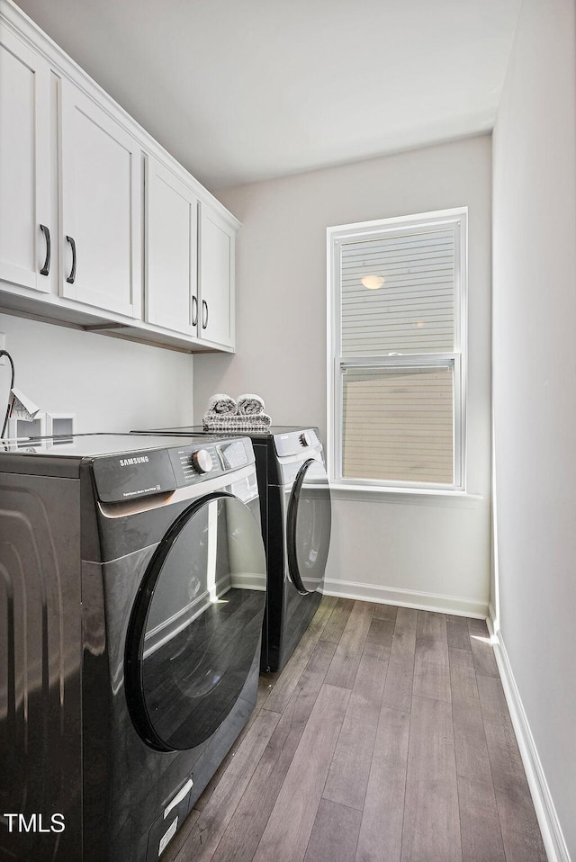 clothes washing area with separate washer and dryer, cabinet space, wood-type flooring, and baseboards