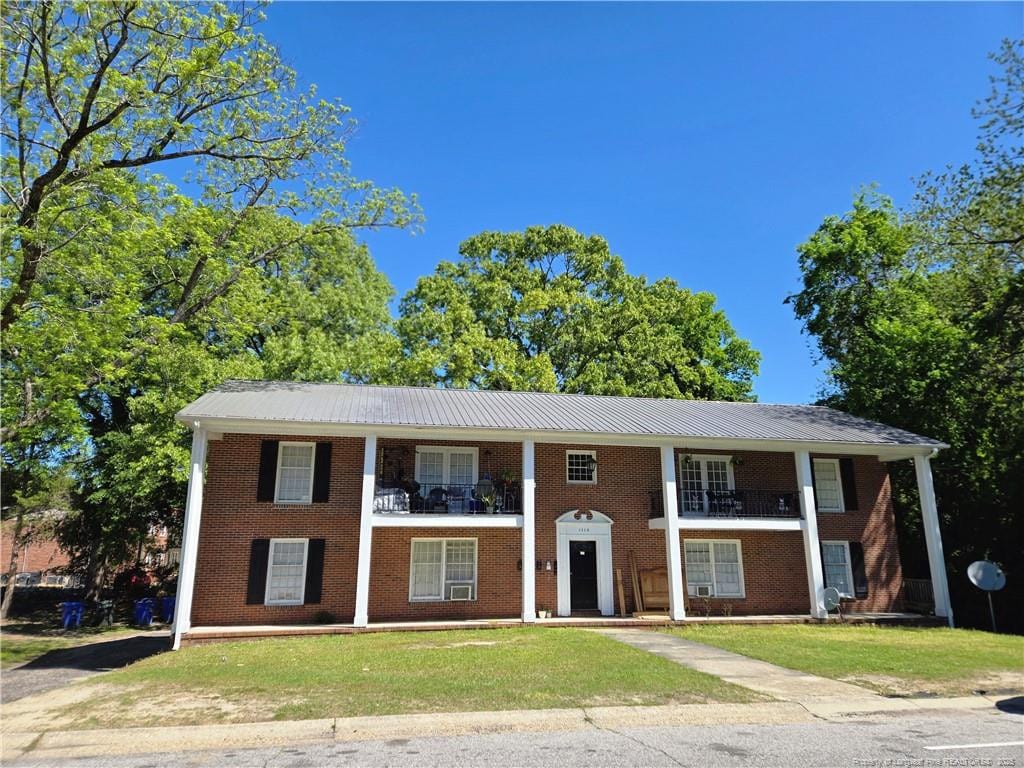 view of front of property featuring brick siding, metal roof, a balcony, and a front yard