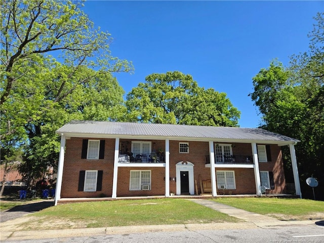 view of front of property featuring brick siding, metal roof, a balcony, and a front yard