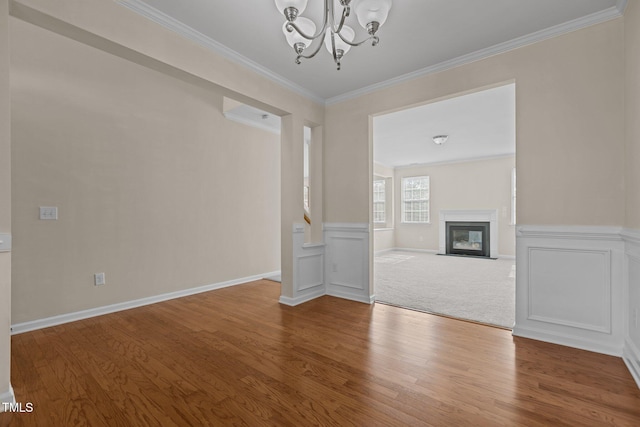 unfurnished dining area featuring wainscoting, a chandelier, a fireplace with flush hearth, wood finished floors, and ornamental molding