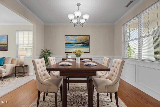 dining space featuring crown molding, a chandelier, visible vents, and light wood-style flooring