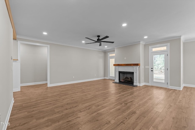 unfurnished living room featuring a ceiling fan, a fireplace with raised hearth, wood finished floors, and ornamental molding