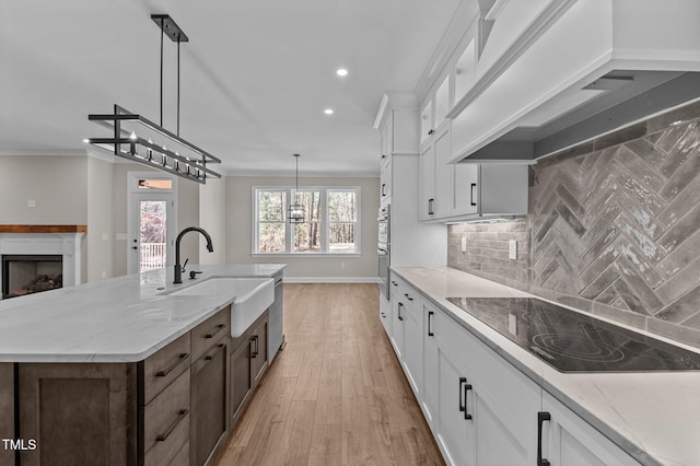 kitchen featuring premium range hood, recessed lighting, black electric cooktop, a sink, and light wood finished floors