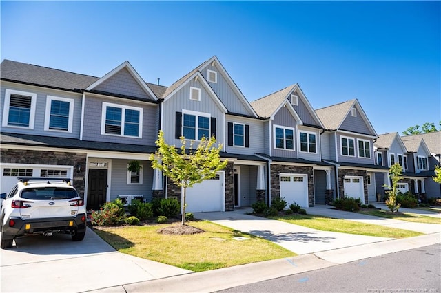 view of property featuring board and batten siding, driveway, a front yard, an attached garage, and stone siding