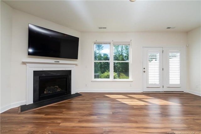 unfurnished living room featuring a fireplace with flush hearth, baseboards, wood finished floors, and visible vents
