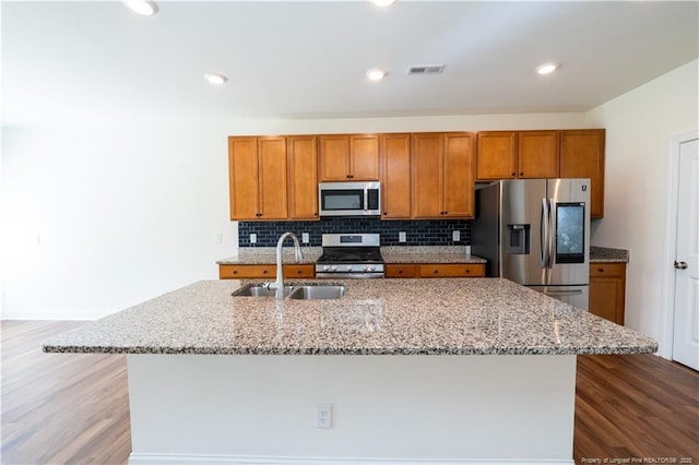 kitchen featuring visible vents, a center island with sink, brown cabinets, a sink, and appliances with stainless steel finishes