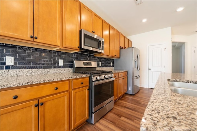 kitchen featuring decorative backsplash, brown cabinets, light stone counters, dark wood-style floors, and stainless steel appliances