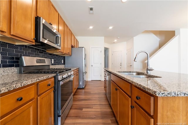 kitchen featuring light stone countertops, dark wood-style floors, a center island with sink, a sink, and appliances with stainless steel finishes