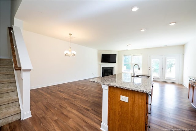 kitchen with a fireplace, a sink, light stone counters, dark wood-style floors, and an inviting chandelier