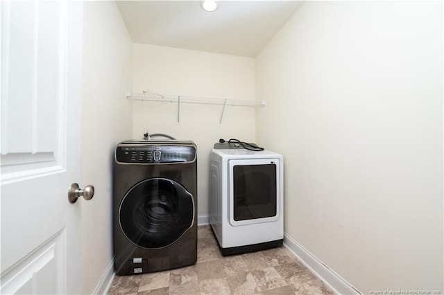 clothes washing area with baseboards, laundry area, stone finish floor, and washing machine and clothes dryer