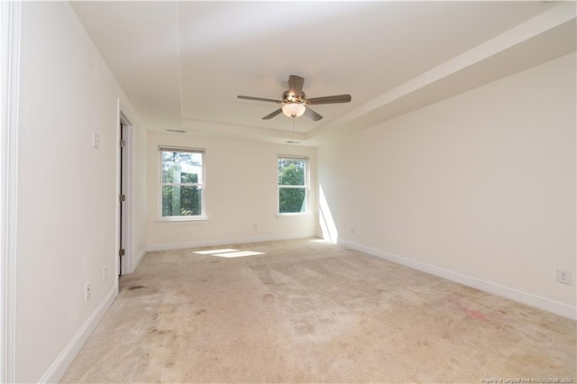 unfurnished room featuring ceiling fan, light carpet, baseboards, and a raised ceiling