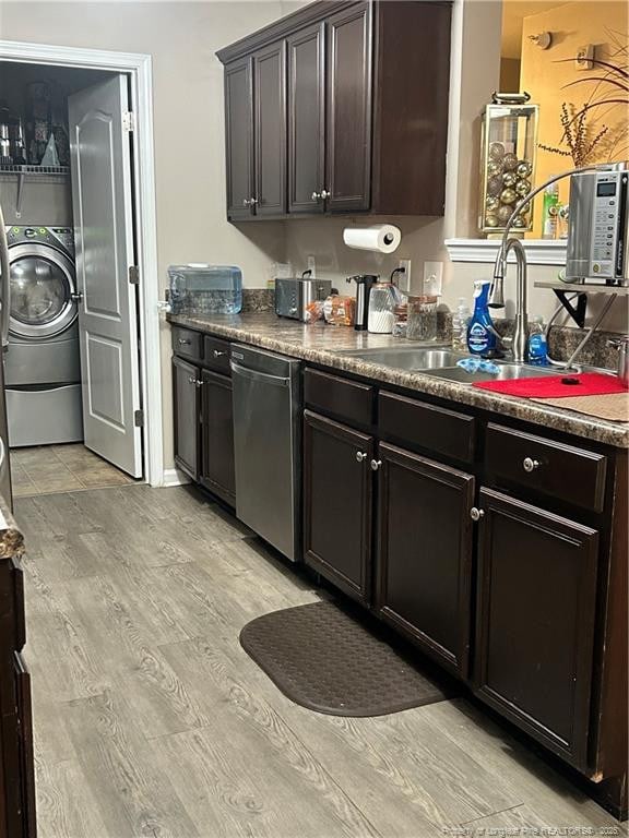 kitchen with dark countertops, light wood-type flooring, dishwasher, a sink, and washer / dryer